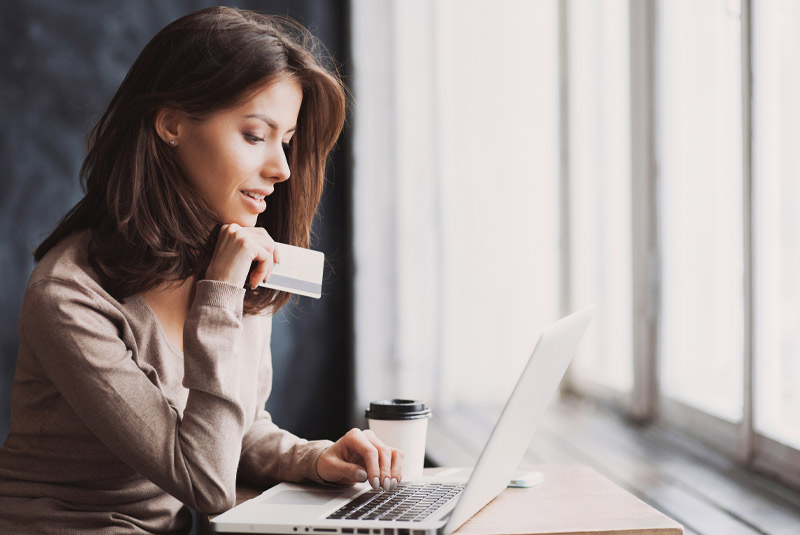 Nice lady with dark hair smiling inputting credit card numbers into laptop for Restore Denture and Implant Center payment