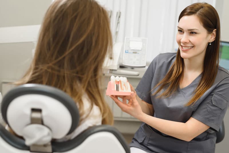 a dental professional showing a patient a dental implant model so she can clearly show what will happen during the dental implant procedure process.